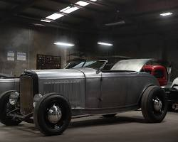 Bare metal 1932 Ford roadster hot rod parked inside a garage with overhead lights