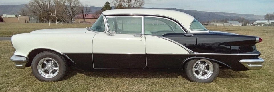 1956 Oldsmobile Super 88 Holiday hardtop shown in side profile with black and white two-tone paint, parked outdoors on grass.