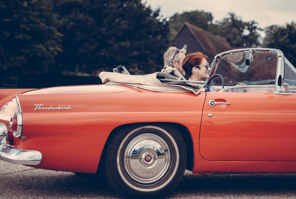 Smiling couple riding in a classic red Ford Thunderbird convertible.